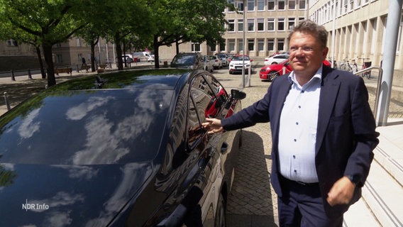 Gesundheitsminister Philipi steht neben seinem Diesel betriebenen Dienstwagen und erklärt dessen Vorzüge für sich. © Screenshot 