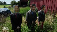 Drei Puppen mit den angehefteten Gesichtern von Olaf Scholz, Robert Habeck und Annalena Baerbock stehen in einem Brennnesselfeld. © Screenshot 