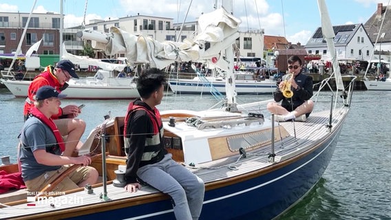Ein Musiker sitzt auf einem Boot und macht Musik mit seiner Trompete. © Screenshot 