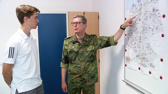 Ein Mann in Uniform zeigt einem Schüler etwas auf einer Karte. © Screenshot 