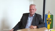 Der Bürgermeister von Teterow sitzt an einem Tisch auf dem die Teterower Flagge steht. © Screenshot 