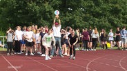 Viele Jugendliche stehen auf einer Laufbahn. Zwei Mädchen laufen los. © Screenshot 