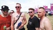 Vier Männer stehen auf einer Festival-Wiese vor einer pinken Bühne. © Screenshot 