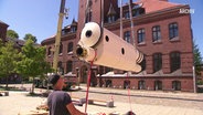 Das sanierte Doppelteleskop der Sternwarte Greifswald wird an Seilen von einem Kran angehoben. © Screenshot 