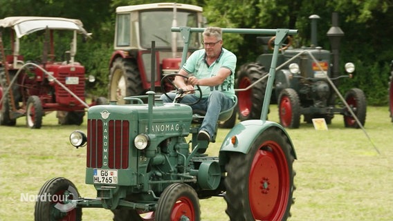 Ein Teilnehmer der Trecker Olympiade fährt einen alten Hanomag-Trecker über eine Wiese. © Screenshot 