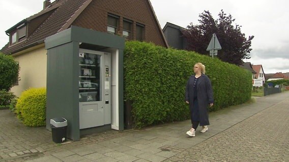 Ein Reporterin nähert sich einem Automaten am Ende einer Hecke © Screenshot 