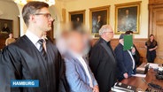 Die Angeklagten stehen mit ihren Verteidigern vor Gericht. © Screenshot 