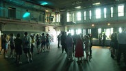 Menschen stehen im Gegenlicht in der neuen Veranstaltungshalle im Grünen Bunker in Hamburg-St. Pauli. © Screenshot 