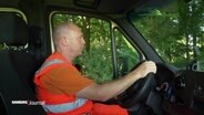 Ein Mitarbeiter der Stadtreinigung sitzt in organgefarbener Arbeitskleidung am Steuer seines Müll-Wagens. © Screenshot 