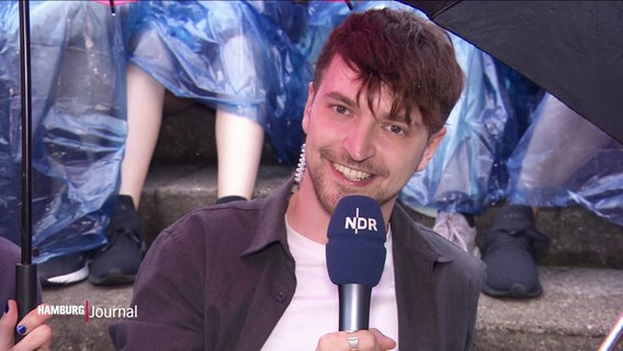 El periodista Tristan Duck está en el estudio informando sobre el ambiente frente al Volkspark Arena, donde se celebra el concierto de Taylor Swift.  © Captura de pantalla 