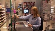 Eine Frau sitzt an der Kasse einer Drogerie. © Screenshot 