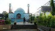 Eine Moschee mit zwei Minaretten, davor ein Polizist. © Screenshot 
