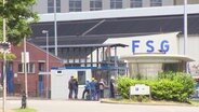 Der Eingangsbereich der FSG, davor ein paar Arbeiter:innen. © Screenshot 