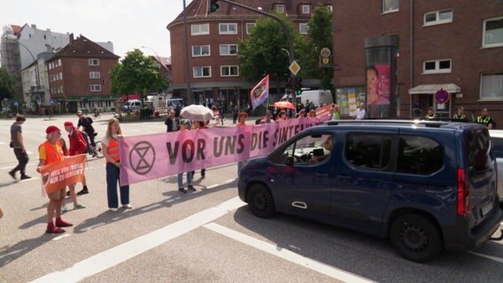 Personen mit einem Protestbanner an einer Straßenkreuzung. © Screenshot 