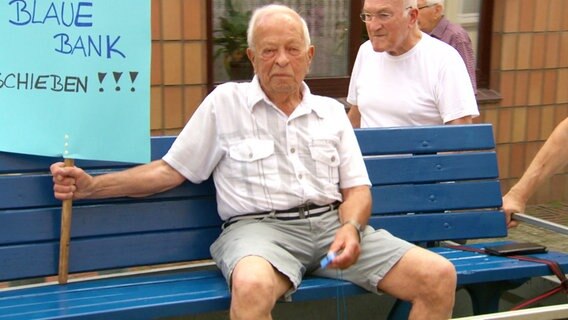 Ein Älterer Mann sitzt auf einer blauen Parkbank. © Screenshot 