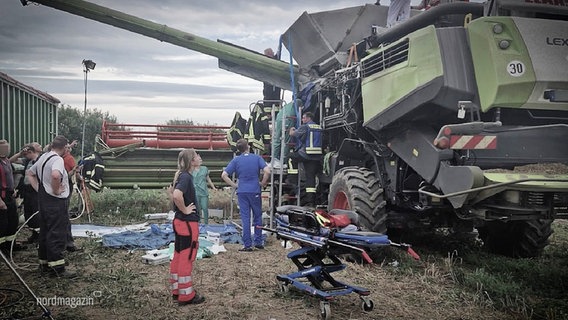 Ein Team von Rettungskräften steht vor einem Mähdrescher auf einem Feld. © Screenshot 