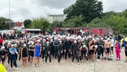Triathletinnen und Triathleten stehen am Strand an der Startlinie. © Screenshot 