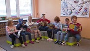 Kinder sitzen mit Büchern in einer Sitzecke in einer Kita. © Screenshot 