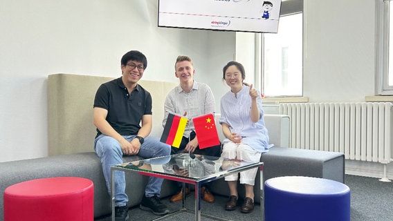 Zwei Männer und eine Frau sitzen hinter einer deutschen und chinesischen Flagge. © Screenshot 