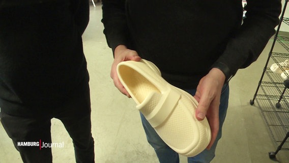 Eine Person hält einen 3D-gedruckten, weißen Schuh aus Thermoplast in die Kamera. © Screenshot 