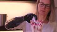 Eine Frau mit einer Handprothese greift einen Strohhalm. © Screenshot 