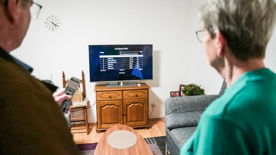 Ein älteres Ehepaar steht vor dem Fernseher. © Screenshot 