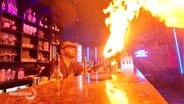 Ein Barkeeper spukt an einer Theke Feuer. © Screenshot 