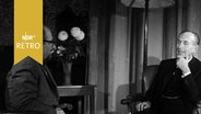 Britischer Außenminister Alec Douglas-Home am 09.12.1960 im Interview am Tisch sitzend. © Screenshot 