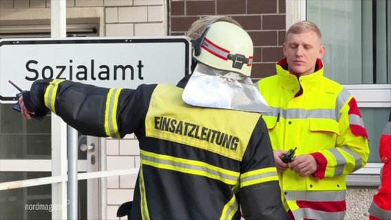 Ein Feuerwehrmann zeigt in Richtung des Sozialamt-Gebäudes. © Screenshot 