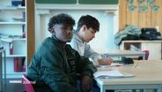 Zwei Schüler sitzen an einem Tisch. © Screenshot 