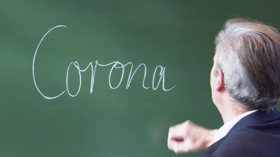 Ein Mann schreibt das Wort "Corona" an eine Tafel. © Screenshot 