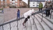 Eine ältere Dame rutscht bäuchlings einen Handlauf hinab. © Screenshot 