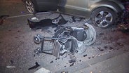 Ein umgeworfener Kinderwagen liegt neben einem stark beschädigten Pkw. © Screenshot 