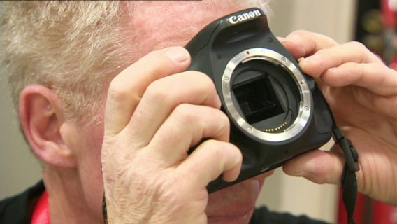 Ein Mann guckt durch einen Fotoapparat ohne Objektiv. © Screenshot 