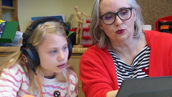 Eine Schülerin trägt große Kopfhörer und schaut mit ihrer Lehrerin auf einen Laptop. © Screenshot 