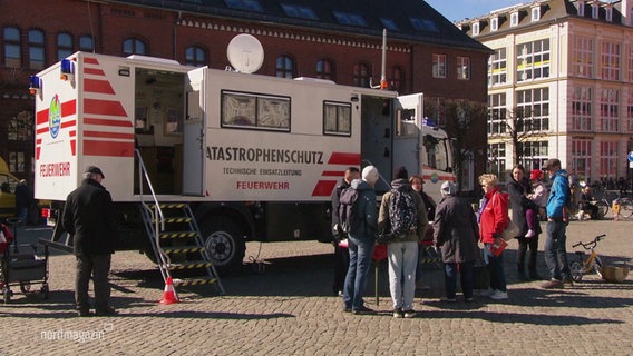 Mehrere Menschen stehen bei einem Einsatzfahrzeug des Katastrophenschutz auf einem Marktplatz. © Screenshot 