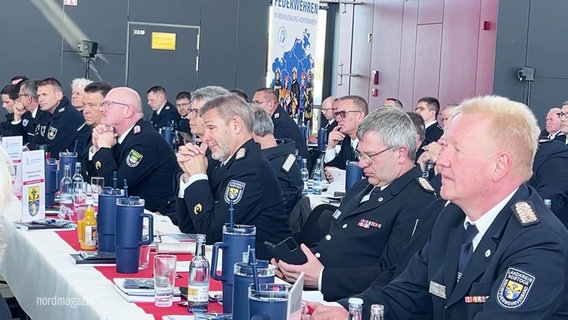 Viele Feuerwehrleiter sitzen in langen Tischreihen bei einer Versammlung. © Screenshot 
