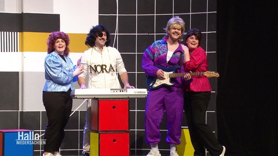 Szene aus "Völlig losgelöst": Schauspielerinnen und Schauspieler im 80-Jahre-Look vor einem Testbild © Screenshot 