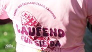 "Laufend für Sie da" steht auf einem T-Shirt einer Sportlerin bei einem Marathon-Lauf. © Screenshot 