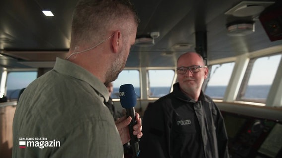Ein Reporter spricht mit einem Kapitän auf eine Polizeiboot. © Screenshot 