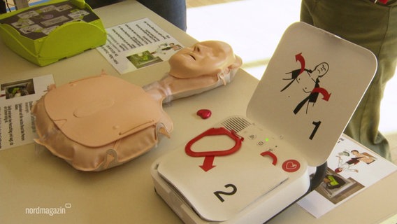 Eine Puppe und ein Defibrillator liegen auf dem Tisch. © Screenshot 