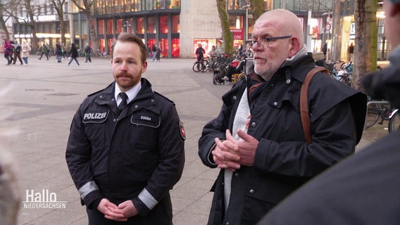 Zwei Männer erklären bei einem Stadtrundgang. Einer trägt eine Polizeiuniform. © Screenshot 