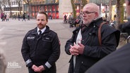 Zwei Männer erklären bei einem Stadtrundgang. Einer trägt eine Polizeiuniform. © Screenshot 