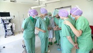 Mehrere Angehörige des Klinikpersonals in Arbeitskleidung blicken auf ein Handy. © Screenshot 