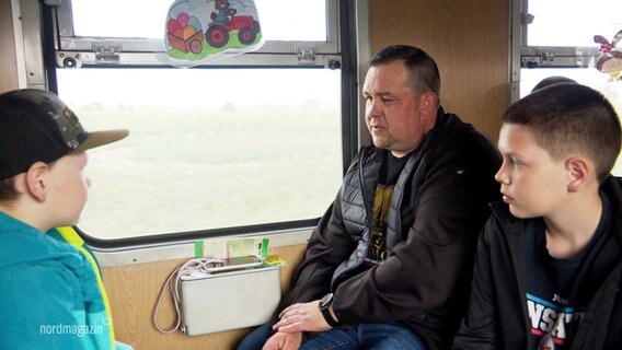 Ein Vater mit seinen zwei jüngeren Söhnen sitzt in einem Eisenbahnwaggon am Fenster. © Screenshot 