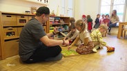 Ein Mann spielt mit mehreren Kindern in der Kita. © Screenshot 