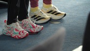 Zwei Personen in Laufschuhen stehen nebeneinander. © Screenshot 