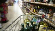 In einem Einkaufswagen sind mehrere Weinflaschen geladen während er durch eine Spirituosenabteilung in einem Supermarkt geschoben wird. © Screenshot 