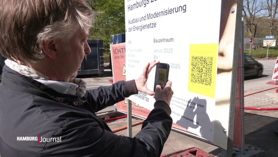 Eine Person scannt einen QR-Code an einem Baustellenschild. © Screenshot 