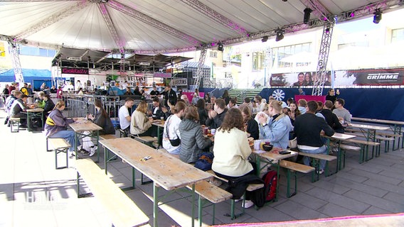 Mehrere Menschen sitzen beim traditionellen "Bingo-Frühstück" des 49. Osnabrücker Terrassenfestes vor einer Bühne. © Screenshot 